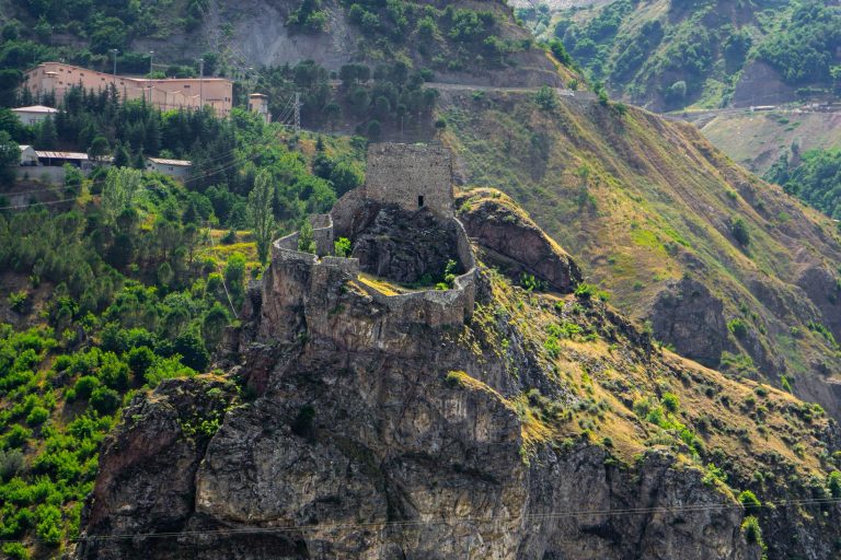 Türkiye'nin Artvin şehrinde, yemyeşil bitki örtüsünün ortasında, kayalık bir tepenin üzerinde yer alan tarihi bir kalenin havadan görünümü.