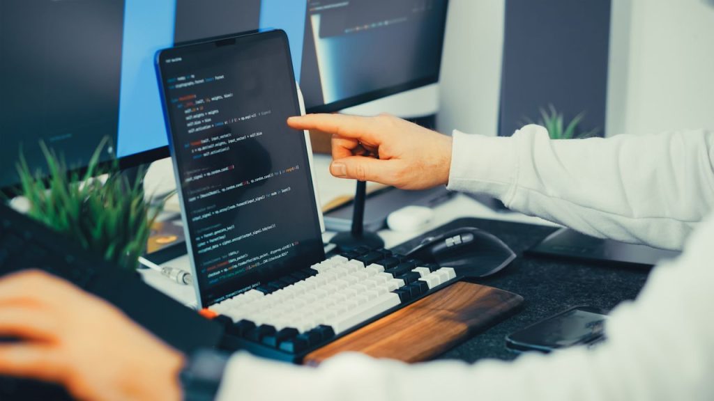 Ofiste laptop ve monitörde kod/otomasyon çalışan kişi