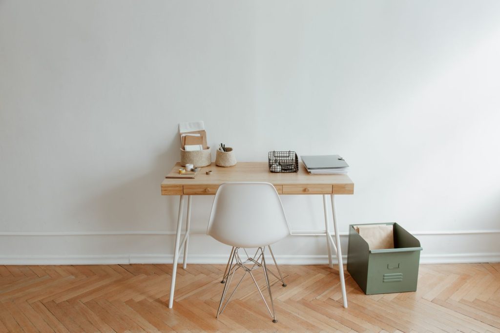 Ahşap bir masa ve beyaz bir sandalye ile minimalist bir ev ofisi kurulumu, temiz ve basit bir estetik sunuyor.