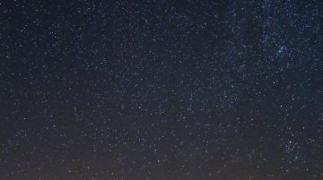 Yıldızlı gökyüzü altında kamp ateşi yanında bir çadır ve insanların olduğu huzurlu bir gece kamp sahnesi.