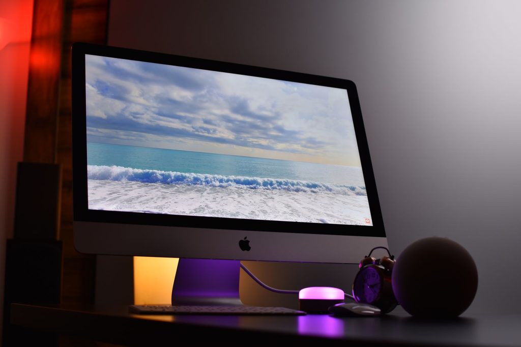Okyanus manzarası gösteren Apple iMac. Ortam aydınlatması ile şık bir çalışma alanı.