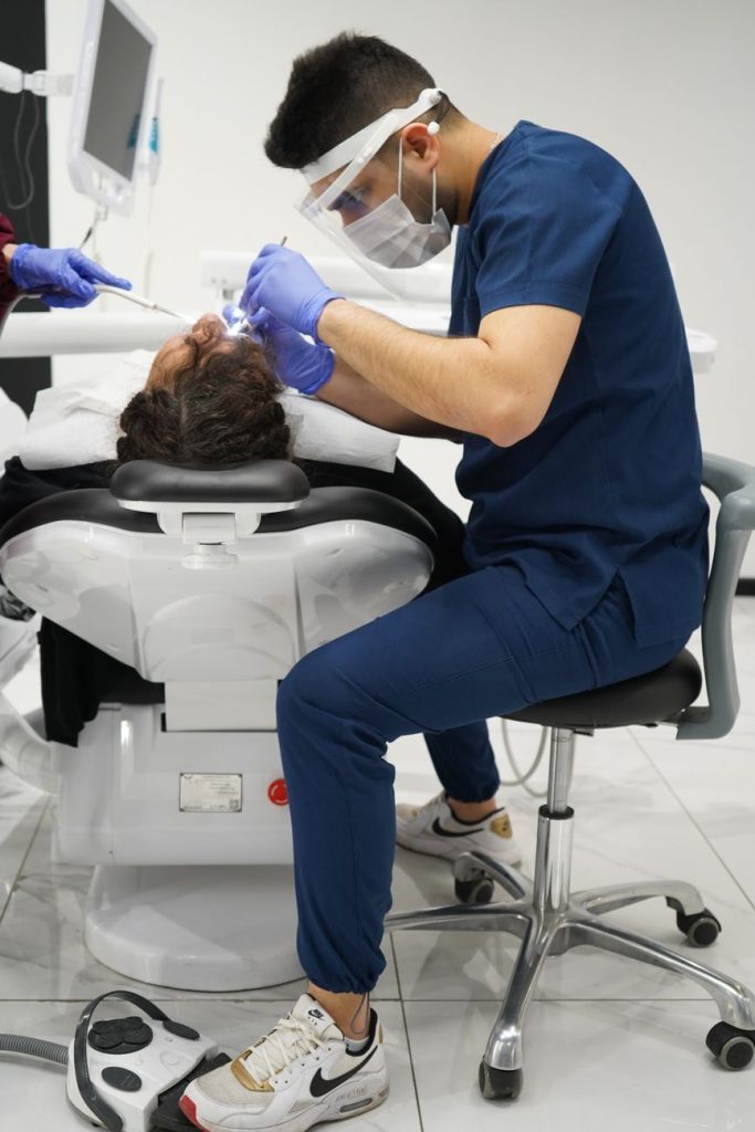 Diş hekimi, modern bir klinikte hastaya tedavi yaparken koruyucu maske ve eldiven giymekte.