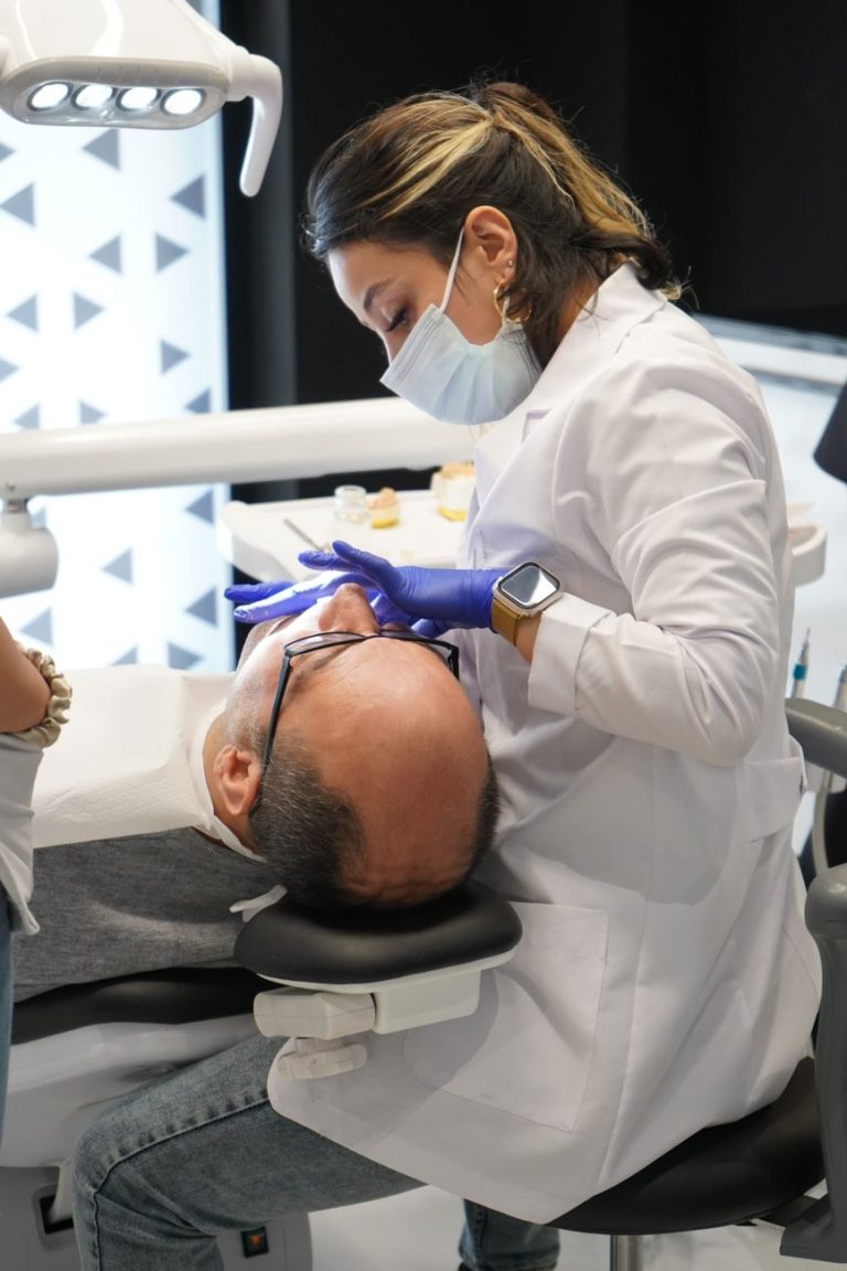 Beyaz önlük giymiş diş hekimi, modern bir klinik ortamında bir hastanın dişlerini muayene ediyor.