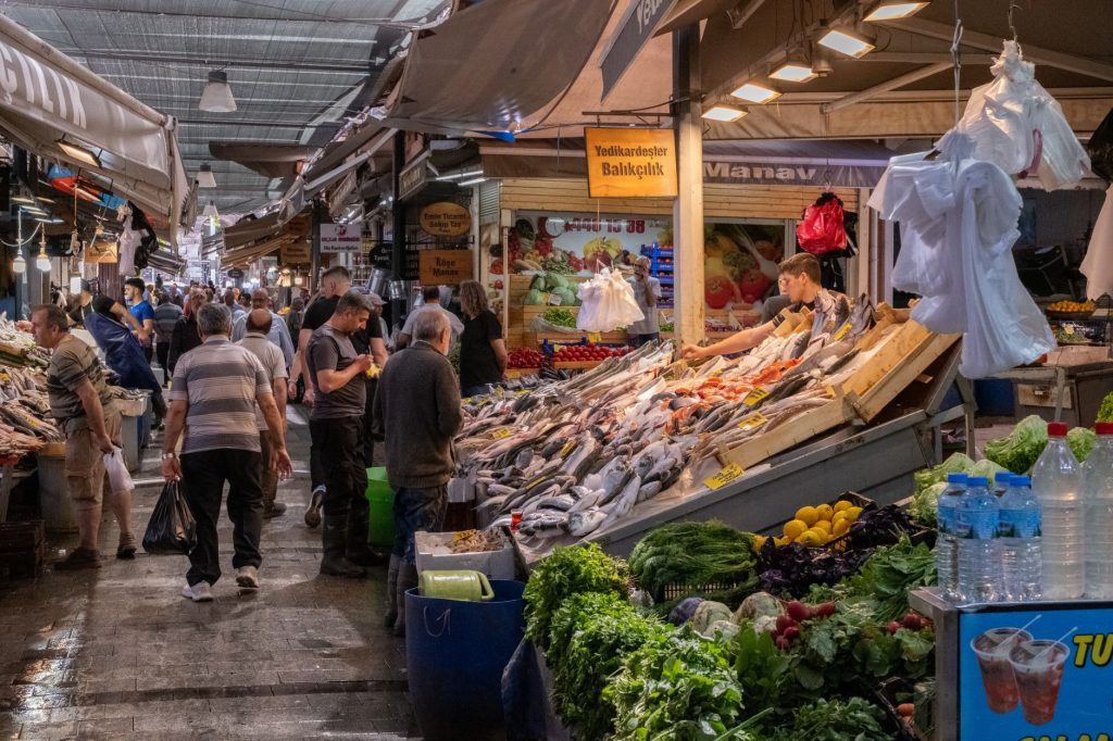 İzmir'deki hareketli bir balık pazarında taze ürünler ve tezgahları gezen alışveriş yapanlar.