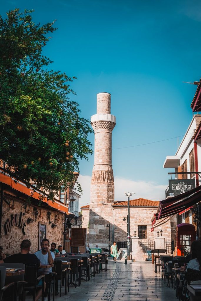 Açık mavi gökyüzünün altında, Antalya, Türkiye'de tarihi bir minareyi içeren canlı bir sokak manzarası.