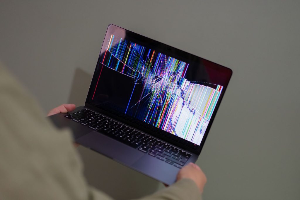 Renkli glitch ile gösterilen kırık bir dizüstü bilgisayar ekranı bir kişi tarafından tutuluyor.
