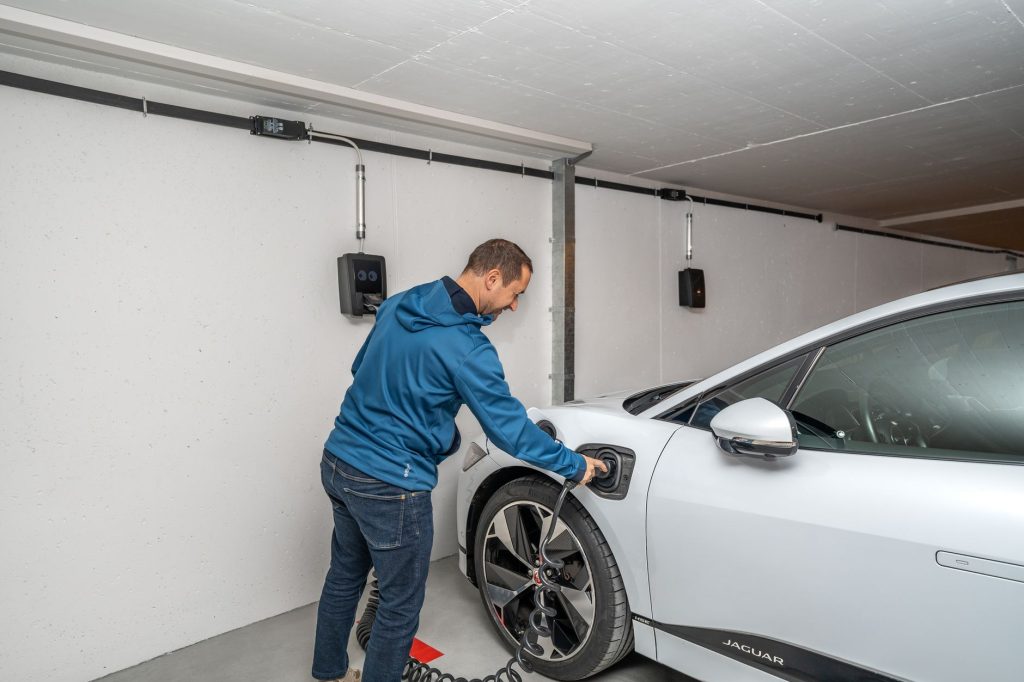 Bir adam, modern bir kapalı garaj ortamında elektrikli arabasını şarj istasyonuna bağlıyor.