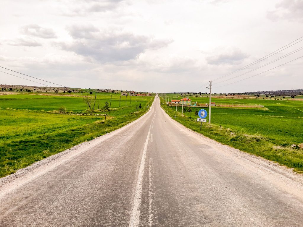 Bulutlu bir gökyüzü altında, yemyeşil Anadolu kırsalını boydan boya geçen dümdüz bir yol.