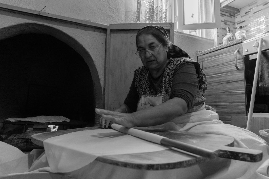 Türk bir kadın, evinin mutfağında odun ateşinde çalışan fırın kullanarak ustalıkla pide hazırlıyor.