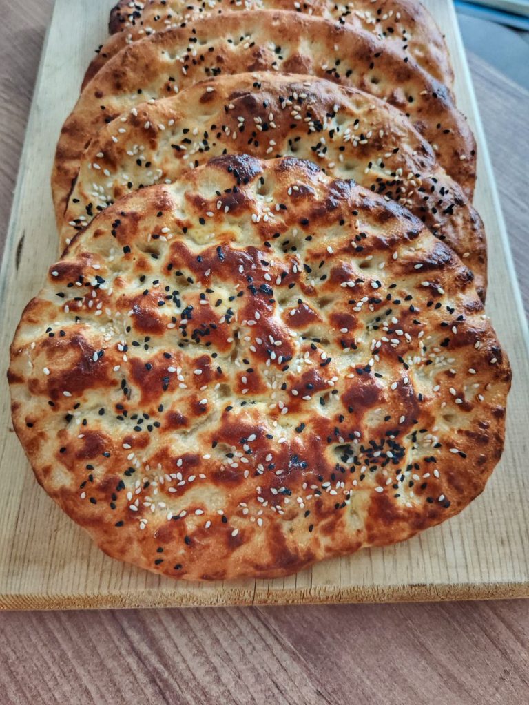 Taze pişmiş, susam ve çörek otu serpilmiş pide ekmekleri, tahta bir tahta üzerinde servis edilir.