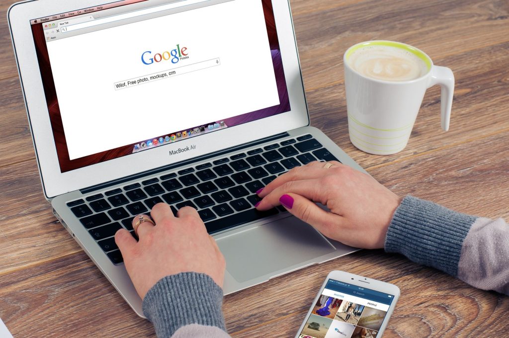 Google arama açıkken MacBook Air'de parmaklar yazıyor, yanında kahve var.