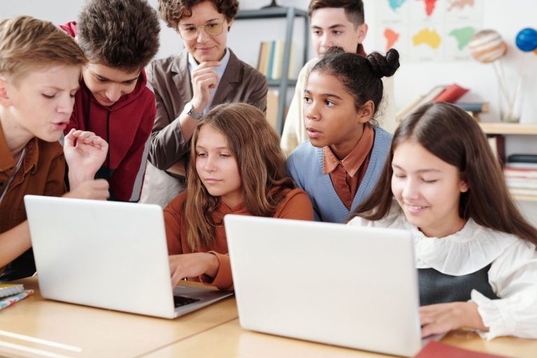 Ergen öğrenciler, öğretmen rehberliğinde eğitim ortamında laptoplarda aktif olarak işbirliği yapıyor.