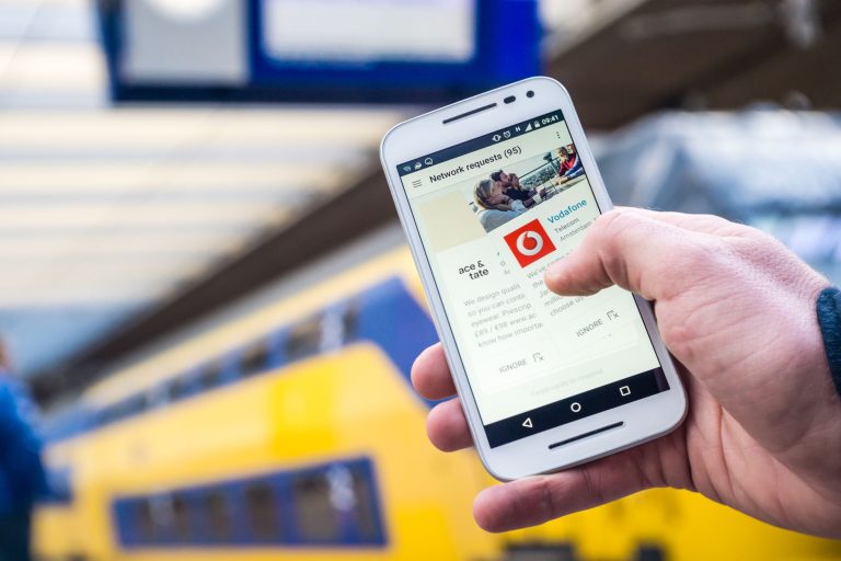 Arka planda trenin olduğu bir ortamda, bir kişinin akıllı telefon kullandığı yakından görünüm.