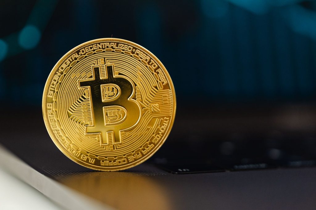 Dijital para birimini temsil eden, dizüstü bilgisayar klavyesinin üzerinde dik duruyor olan altın Bitcoin madeni para.