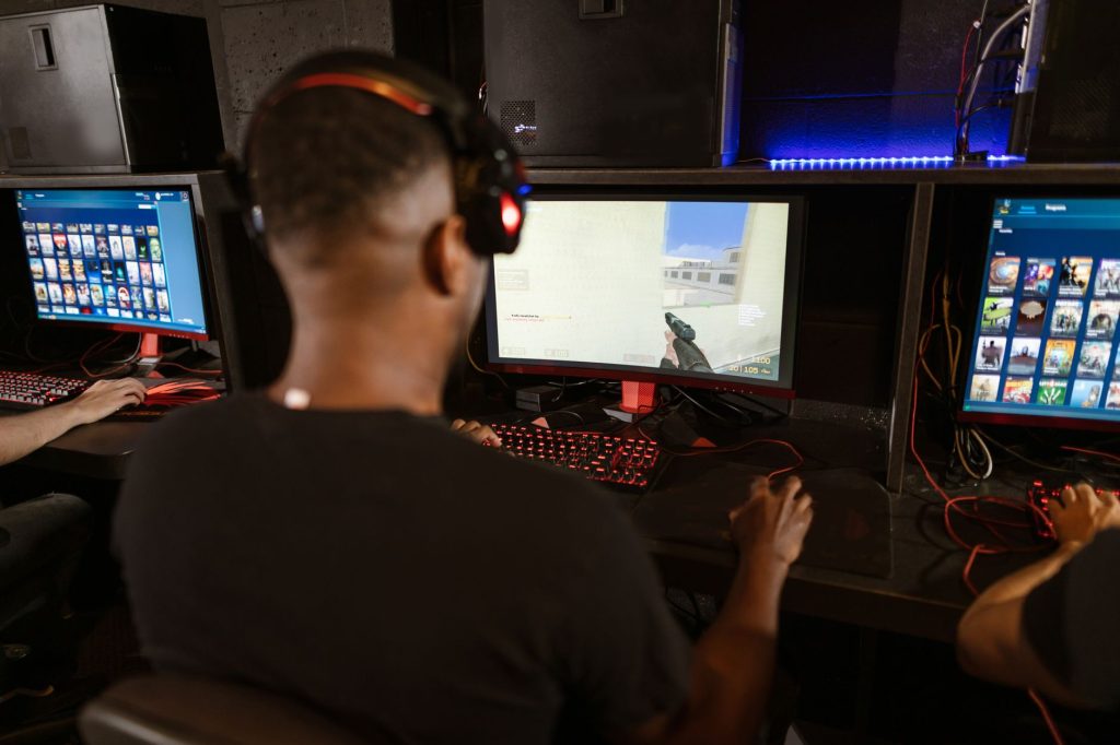 Bir adam, birden fazla ekran bulunan modern bir esports kurulumunda derin bir video oyununa dalmış.