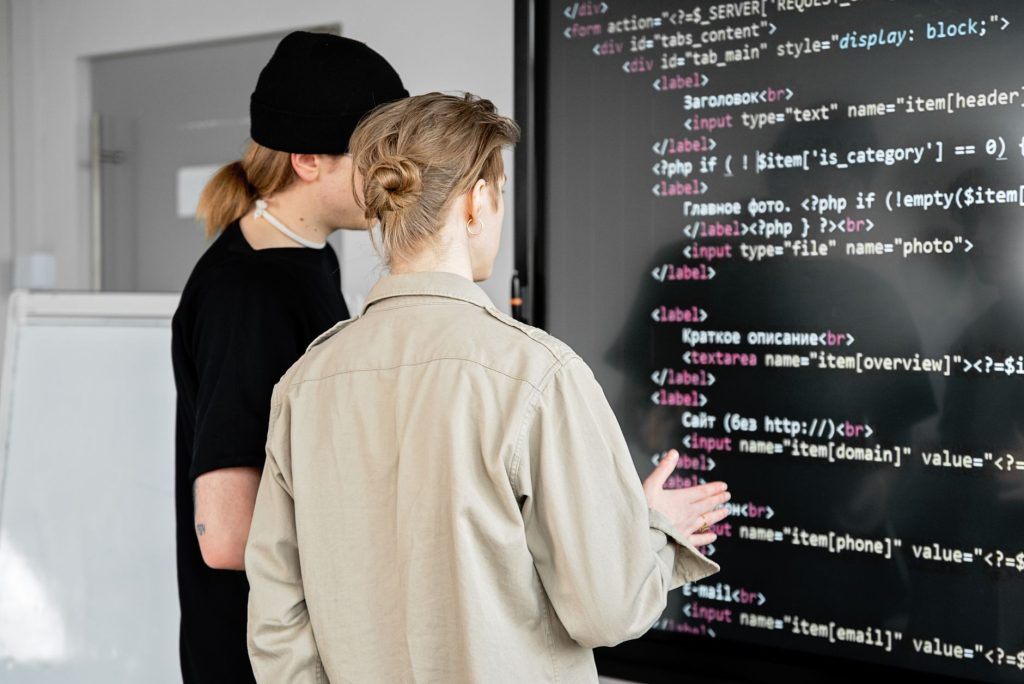 İki geliştirici, modern bir ofis alanında büyük bir ekranda kodu inceliyor, web geliştirmeye odaklanıyor.