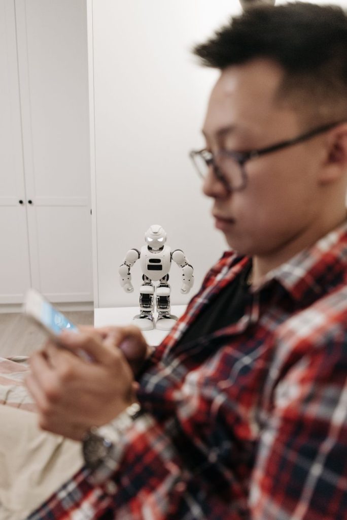 Adamın arka planda robotla birlikte akıllı telefona odaklandığı, modern teknolojiyi temsil eden bir görüntü.