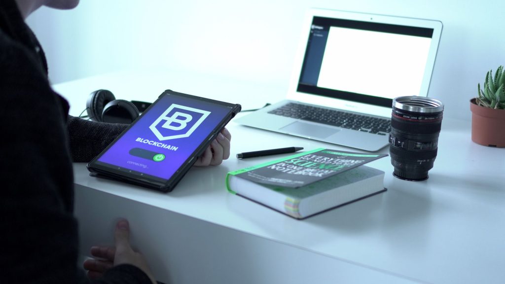 Blockchain gösteren tablet, dizüstü bilgisayar, kitap ve kamera lensi ile dolu bir masa, teknoloji ve yeniliği simgeliyor.